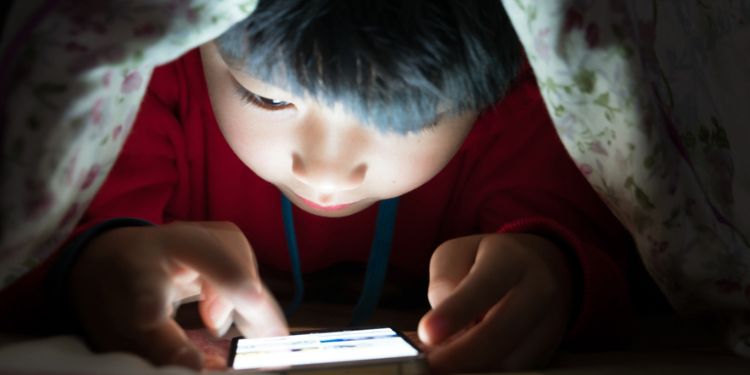 布団の中で明るい画面をみる子どものイメージ