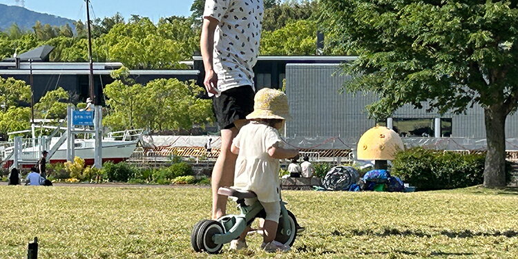 三輪車に乗る子を見守る親